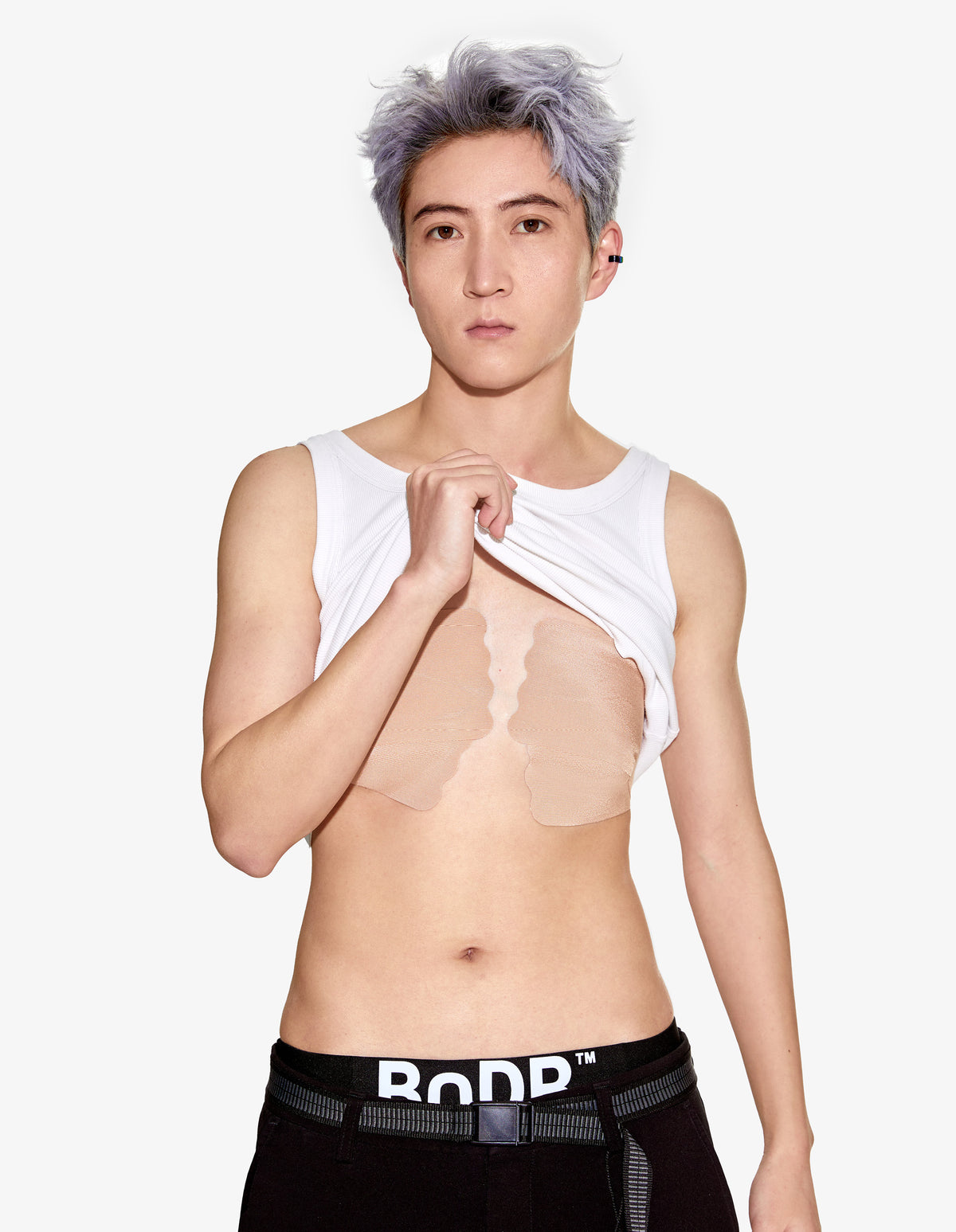 BnDR chest binding tape. model lifting a white tank to reveal beige tape on the chest.